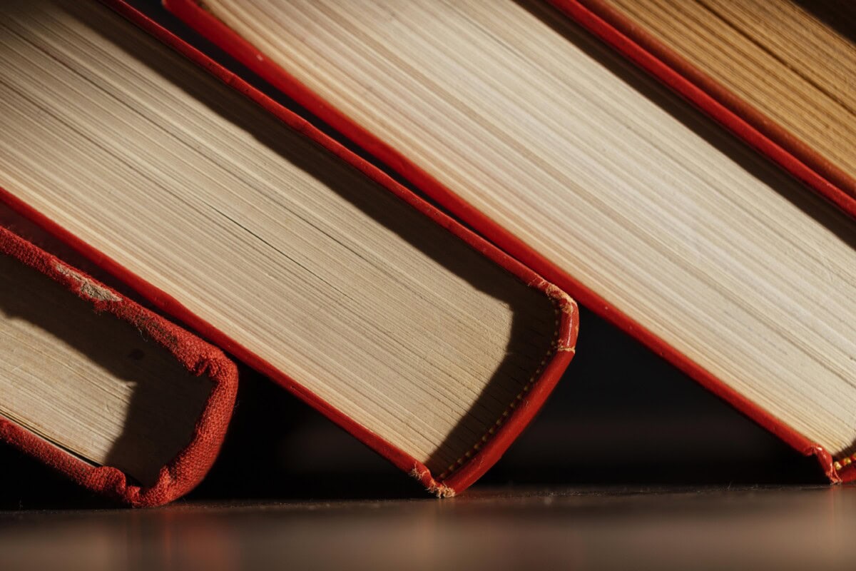 Close-up view of the spines and pages of four books with red covers, arranged at an angle and resting on a reflective surface.