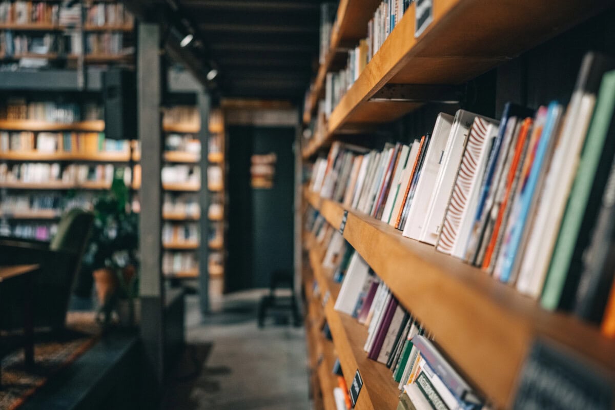 A close-up view of bookshelves filled with books in a library or bookstore, with soft lighting and a blurred background.