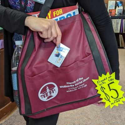 A person holds a library card while carrying a maroon Friends of the Whitinsville Social Library tote bag with books; a $5 price tag is attached.